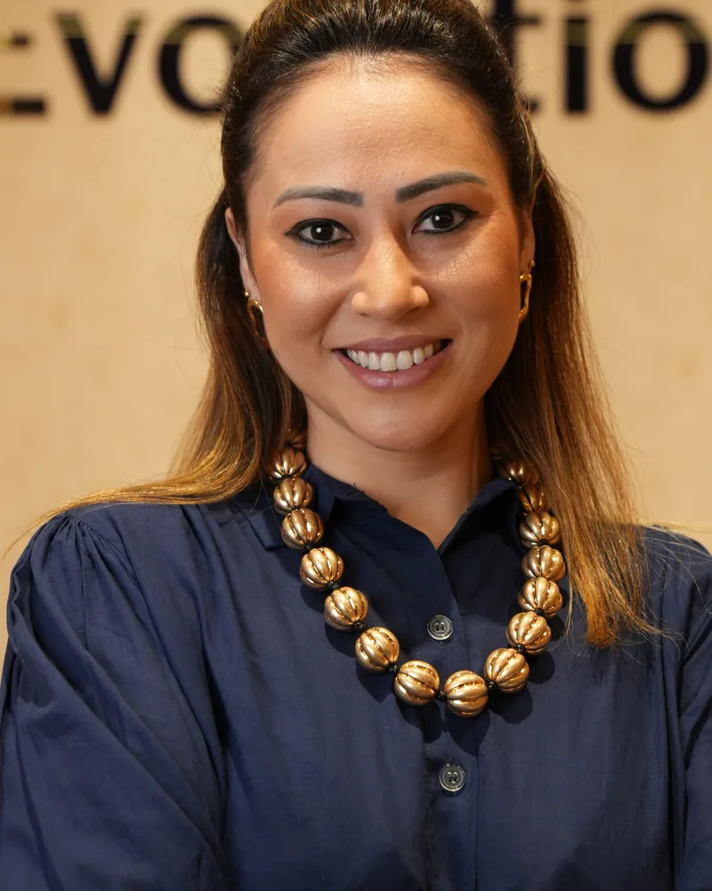 Dra. Thays Tamaributi de blusa azul-marinho, diante do letreiro do Instituto Evollution